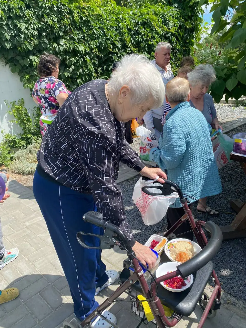 Жінка з ходунками отримує обід на подвірʼї